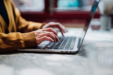 A close-up photo of a woman's hands typing on a laptop computer.