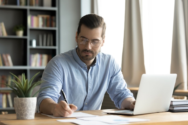 Focused man working on laptop making notes