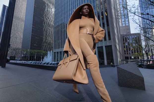 Model wearing Michael Kors designs walking through a city.
