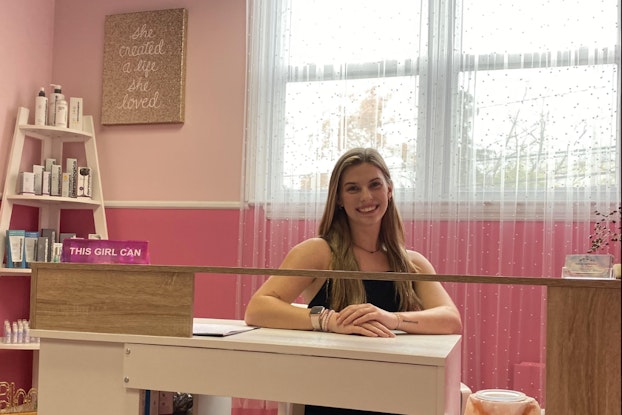  Smiling young business owner stands behind the front desk at her shop.