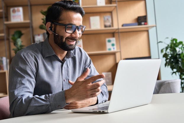 Business person wearing headset, talking at virtual meeting.