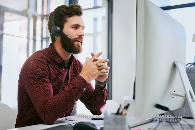 Businessman sitting sitting at desk, having discussion on a headset while using a computer in the office.