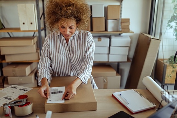 Woman placing a shipping label on a package in her workshop.