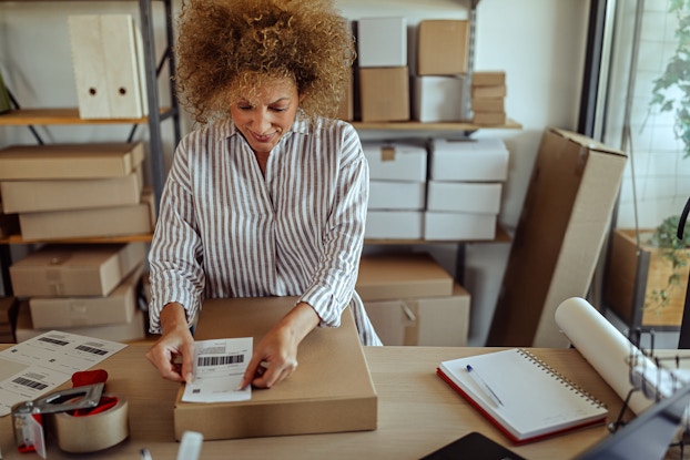  Woman placing a shipping label on a package in her workshop.