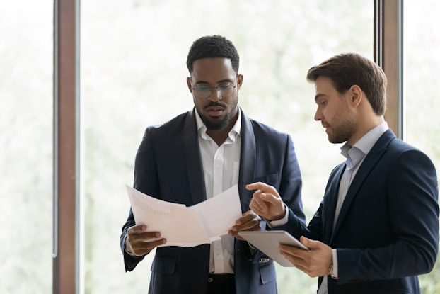 Businessman consults a colleague about the content of a piece of paperwork.
