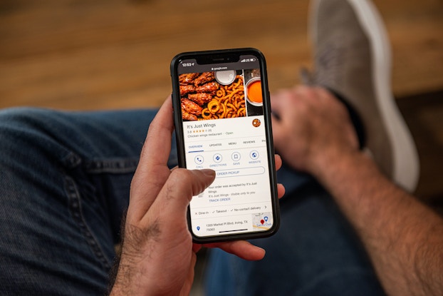  Person holding phone ordering It's Just Wings through a food delivery app.