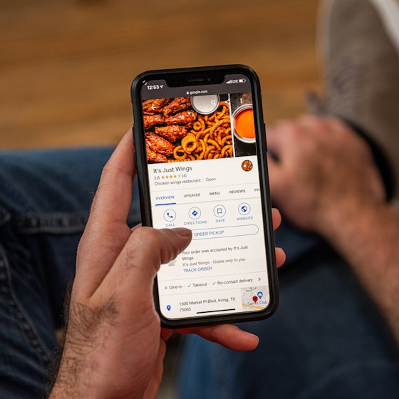  Person holding phone ordering It's Just Wings through a food delivery app. 