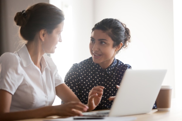 Two young professional women meet and discuss a strategy while at a laptop computer.