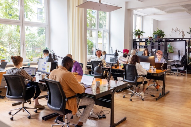  Open-plan office with employees working at stations at long tables.