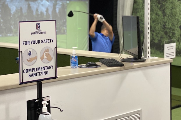 Golf simulator next to complimentary hand sanitizer at a PGA TOUR Superstore location.