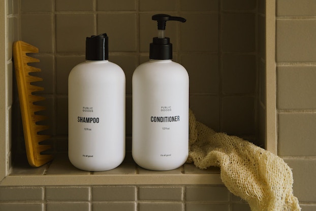  Public Goods' brand shampoo and conditioner positioned in a tiled shower with a washcloth.