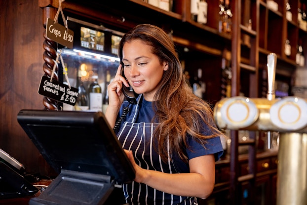  Waitress working at a pub and talking on the phone taking a delivery order.