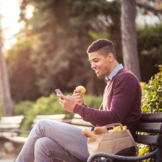  Man eating a snack while checking his phone in a park 