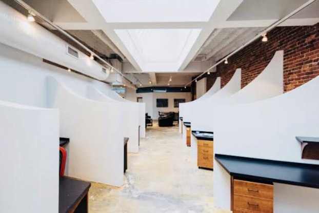  A modern co-working office space shows individual desks with partitions, modern lighting and an exposed brick wall.