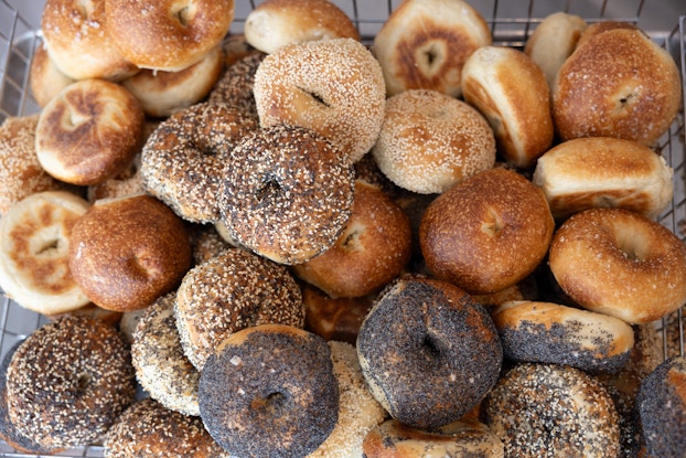 A close-up of a pile of bagels, some plain and some covered with poppy seeds, sesame seeds, or everything seasoning.