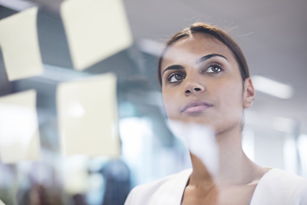 Woman at work considers her tasks as she makes notes on sticky notes.