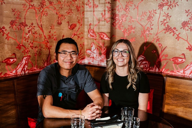  Queen's English co-owners Henji Cheung and Sarah Thompson sitting at a table in their restaurant.