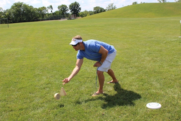 A man rolls a ball on a large, grassy space on a sunny day