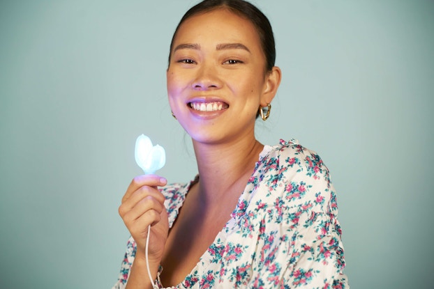  Woman smiling while holding a teeth whitening device by SNOW.