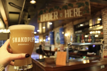  Person holding up a beer with the interior of Shakopee Brewhall in the background. 