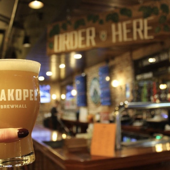 Person holding up a beer with the interior of Shakopee Brewhall in the background.