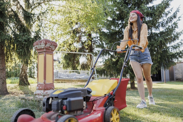 Teenager uses a lawnmower in a backyard.