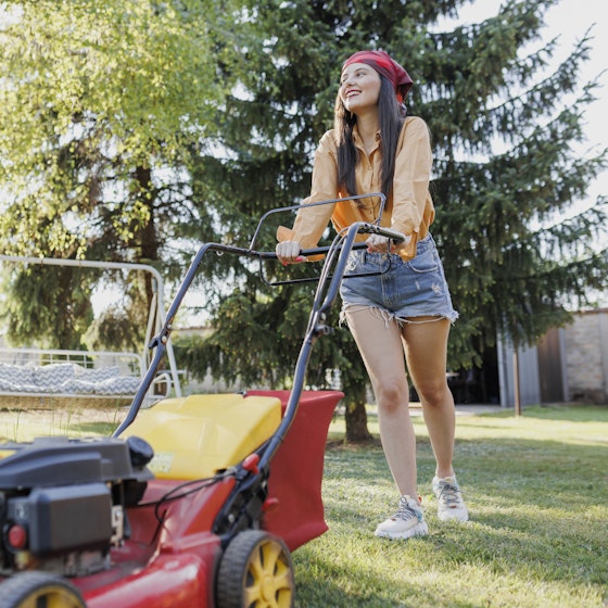 Teenager uses a lawnmower in a backyard.