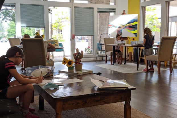 Children create art in an art studio with plentiful windows and natural sunlight.