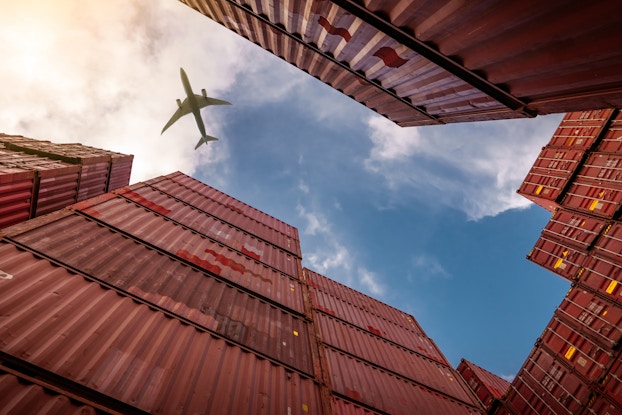 Plane flies above shipping containers at industrial port