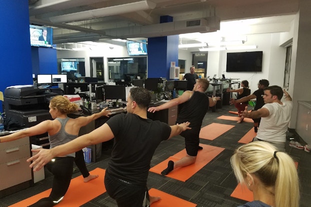  Coworkers participate in group yoga class in modern office