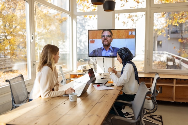 Business colleagues having a video conference. Two colleagues are in a conference room and another is on a video call.