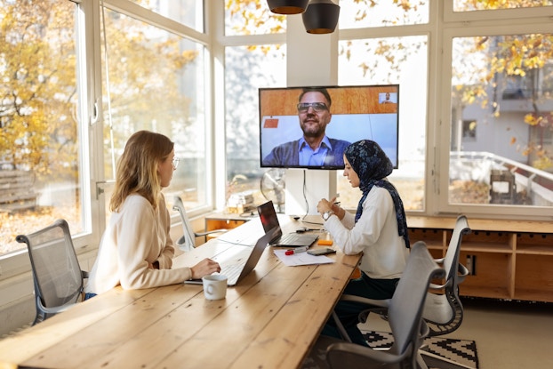  Business colleagues having a video conference. Two colleagues are in a conference room and another is on a video call.