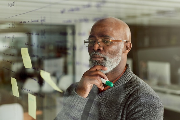  Cropped shot of a mature businessman brainstorming with notes on a glass wall