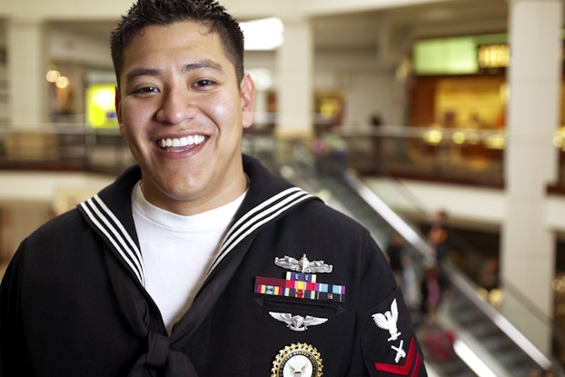  U.S. male sailor pictured smiling with a mall in the background.