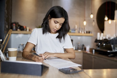  Woman business owner completes paperwork behind the register of her shop. 