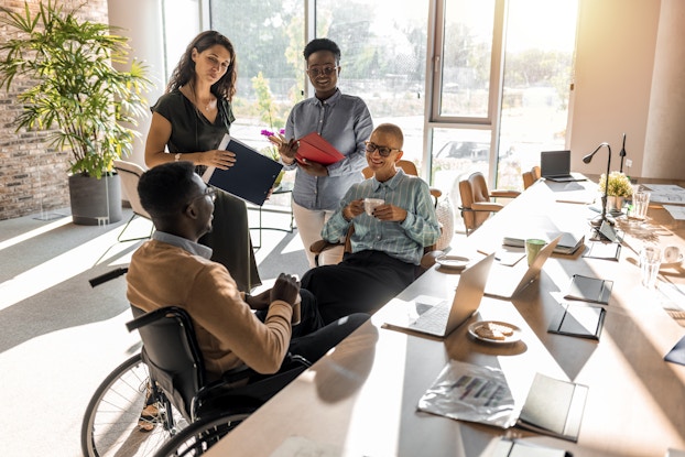A diverse group of employees gather and talk in a well-lit, open office