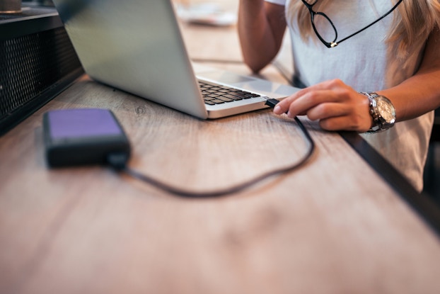  A woman plugs an external hard drive into her laptop.