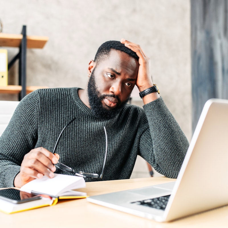 Frustrated man holds glasses and looks at laptop in an office.