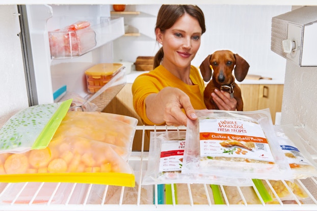 Woman holding her dog while she reaches into her freezer for a frozen pet meal.