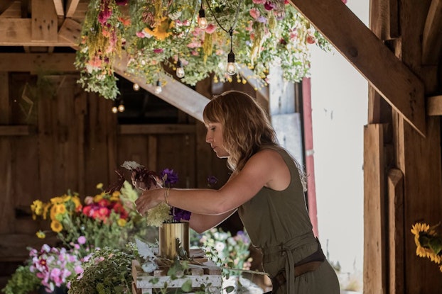 Woman creates a flower arrangement in a rustic farmhouse room.