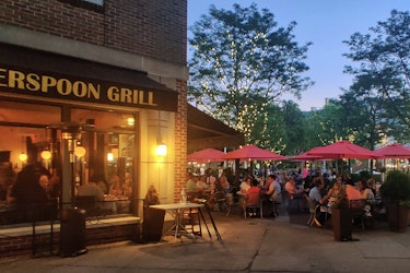  Busting restaurant at dusk hosts a dining room and outdoor patio filled with guests. 