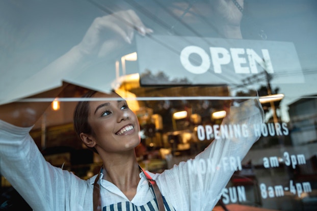  woman hanging an open sign on door of business