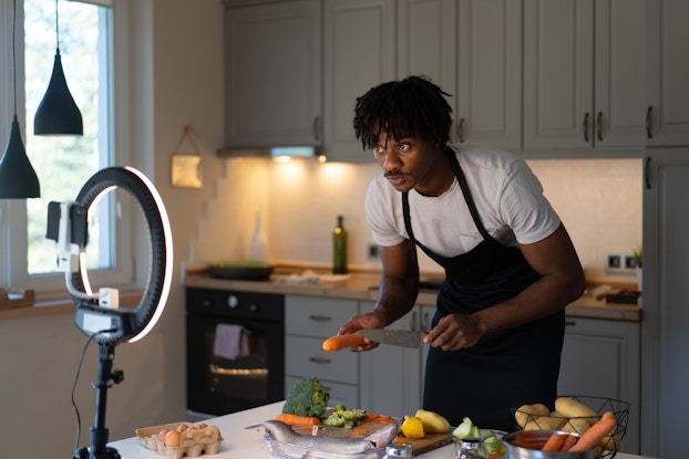  Man wearing an apron in his kitchen, recording himself preparing food.