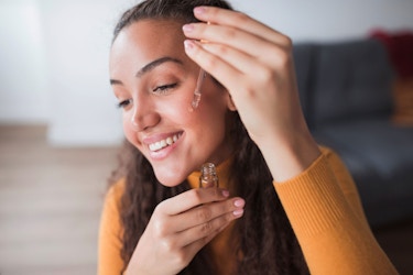  A close-up image of a young woman influencer applying a beauty serum to her cheeks. 