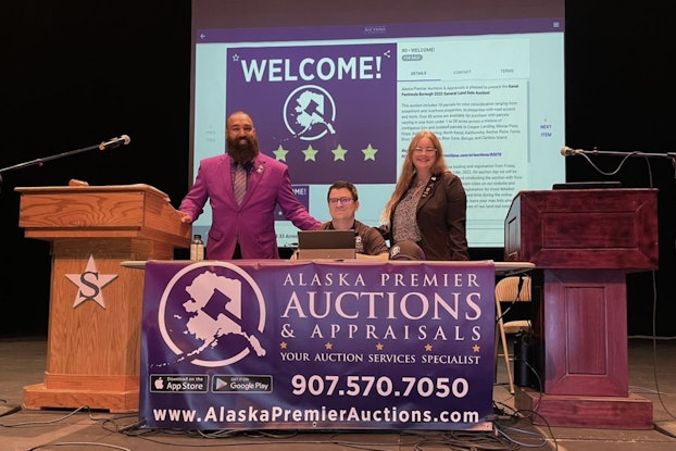  Three people from Alaska Premier Auctions and Appraisals on stage next to podiums.