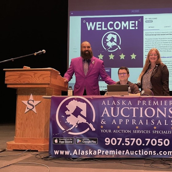 Three people from Alaska Premier Auctions and Appraisals on stage next to podiums.