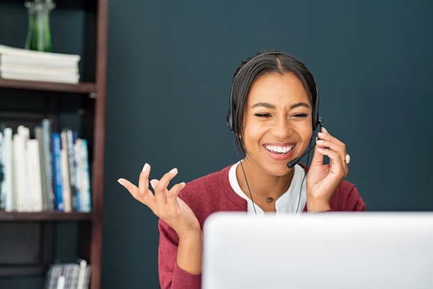 Happy woman working remotely in front of a computer screen wearing a headset.