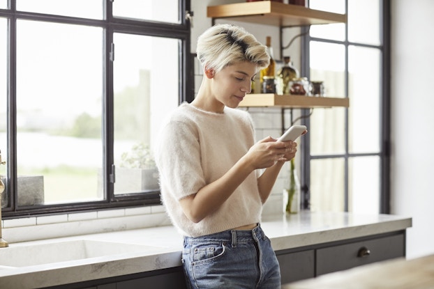 Woman standing inside her home on her phone.