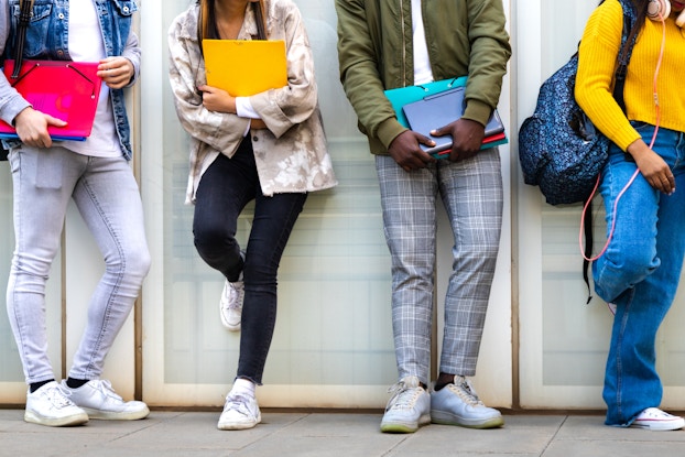 Group of teens standing in a row and holding school supplies.