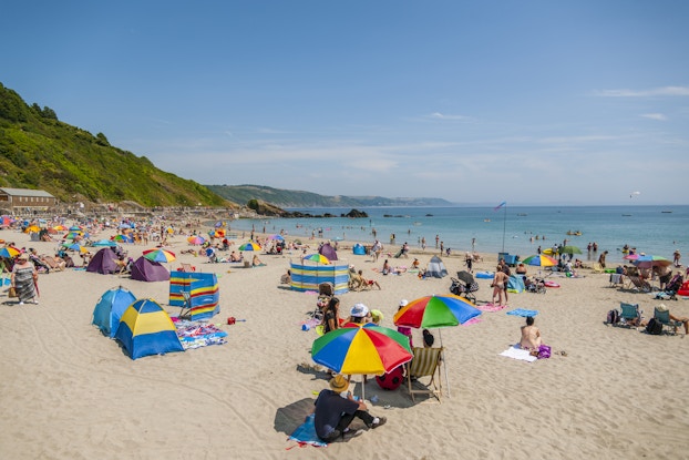 Beachgoers on a beach on a sunny day with colorful umbrellas and gear.